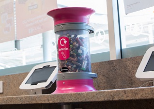 C-Thru 5L Battery Recycling Container with magenta lid and graphic on worktop with electronic tablets