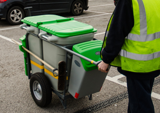 Double Space-Liner™ Orderly Barrow in grey with two compartments with green lids and detailing and operator wearing high-visibility jacket pushing the cart