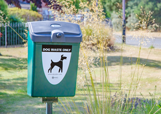 Fido™ 25 Dog Waste Bin in deep green with post-mounted fixings situated in public area
