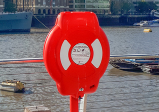 Guardian™ Lifebuoy Housing in red with white instruction graphic in front of large river with boats