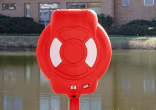 Guardian™ lifebuoy housing water safety equipment in red, situated by lake on school grounds