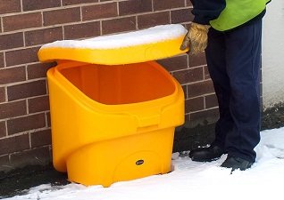 Nestor™ 90 Grit Salt Bin in yellow with snow on lid and operator opening bin on snowy ground