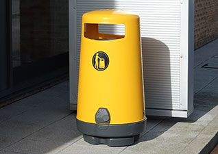 Topsy™ 2000 Outdoor Litter Bin in yellow situated by airport building